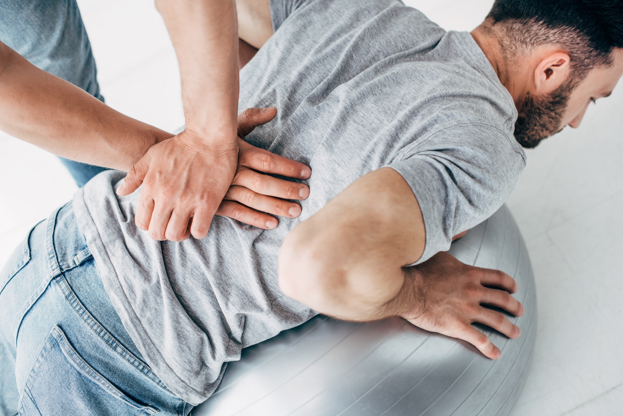 chiropractor massaging back of man lying on fitness ball