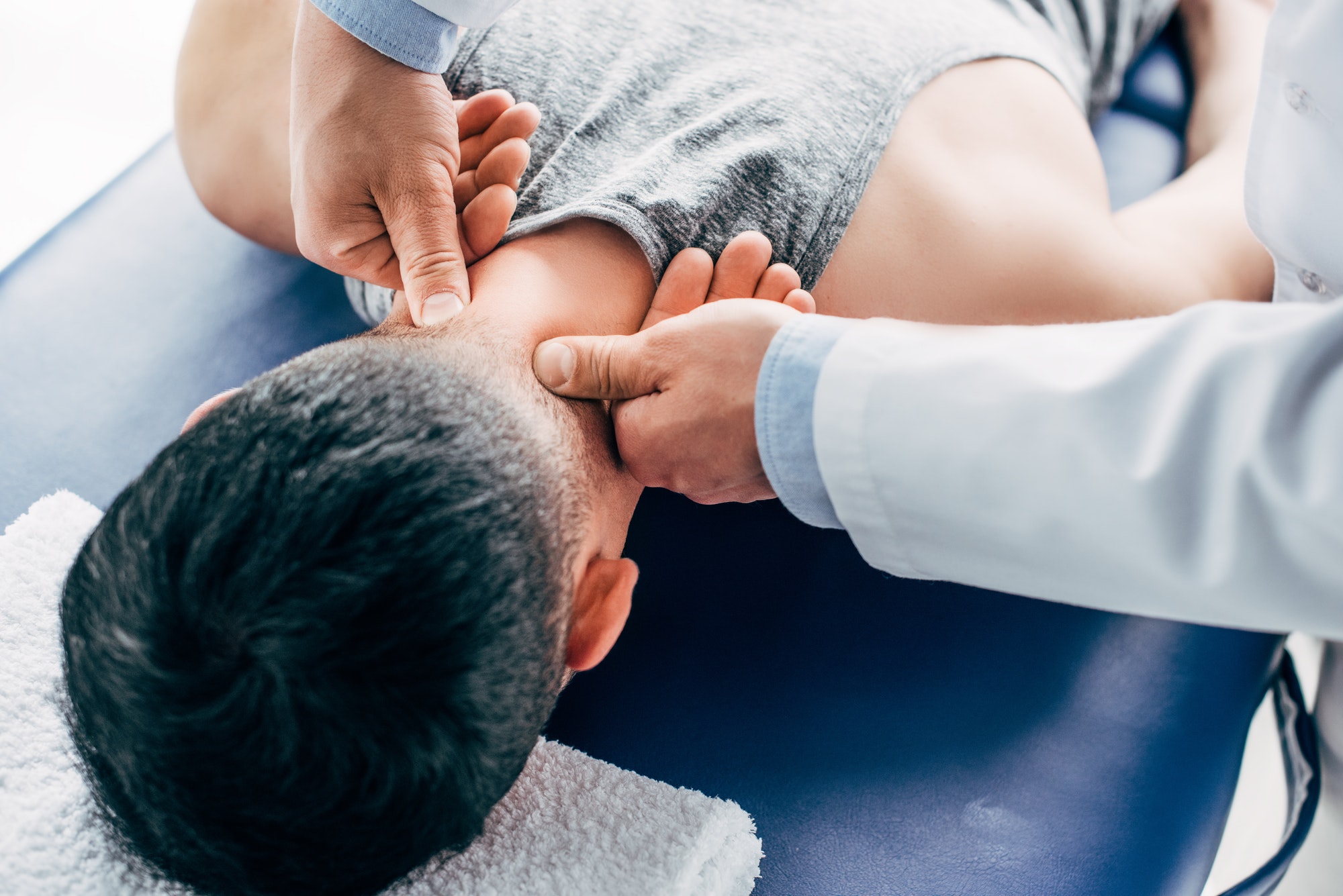 chiropractor massaging neck of man lying on Massage Table with towel